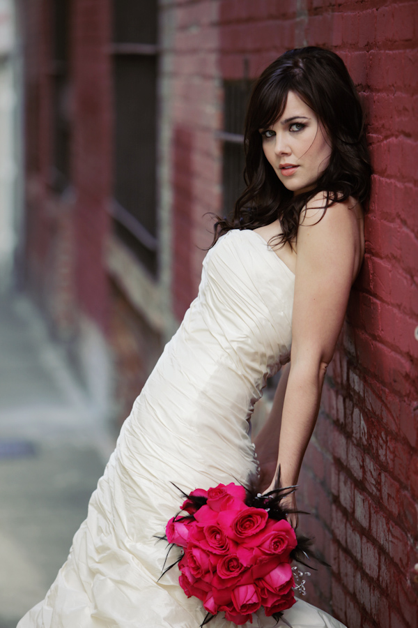 Beautiful bride leaning against a red brick wall holding dark pink roses -photo by San Francisco based wedding photographer